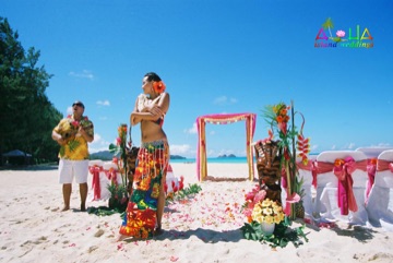 Hula dancer in a colorful skirt beside a carved tiki at a beach wedding